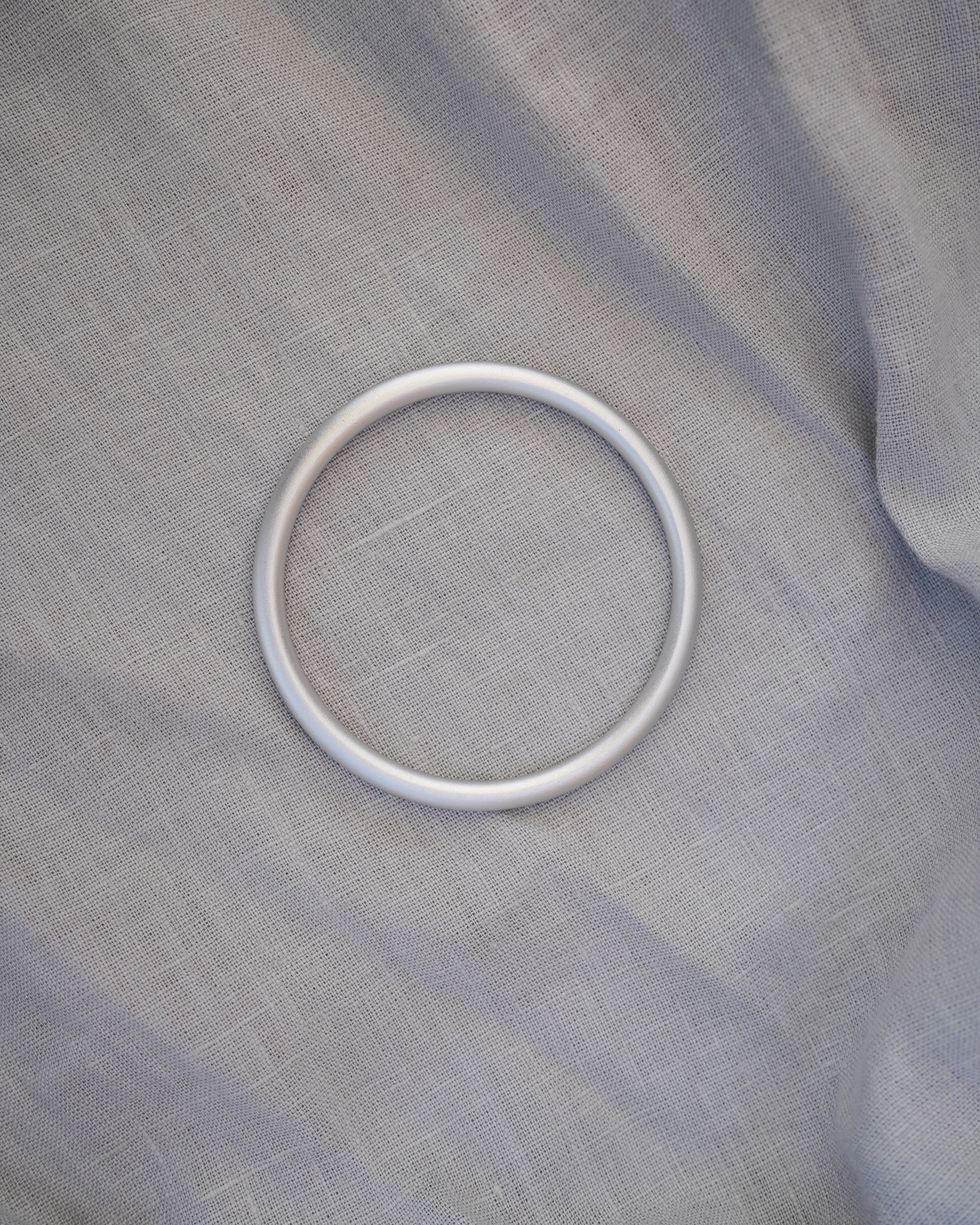 Ein silberner Ring liegt auf einer hellgrauen Ring Sling